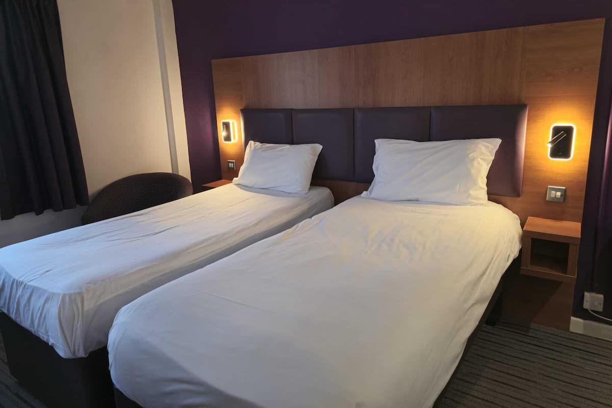 A hotel room with two single beds, a wooden headboard, and bedside lamps.