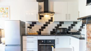 Een kleine keuken met witte kasten, een zwarte oven, een magnetron en een gasfornuis.