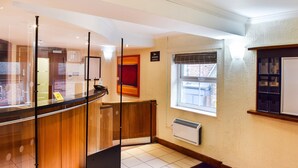 Een receptiegedeelte met een glazen scheidingswand, een receptiebalie, een raam met zonwering, een radiator en een bord aan de muur.