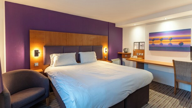 Een hotelkamer met een groot bed, een bureau, een stoel en een schilderij aan de muur.