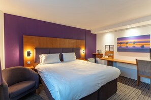 Habitación de hotel con una cama grande, un escritorio, una silla y un cuadro en la pared.