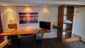 Een moderne kamer met een houten bureau, een computer, een stoel, een schilderij, een koffieapparaat en een plank.