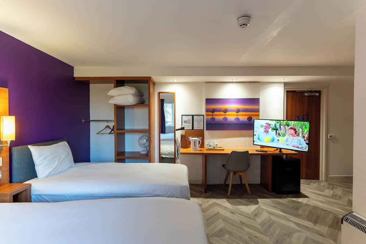 A hotel room with two beds, a desk with a chair, a television, and a wardrobe.