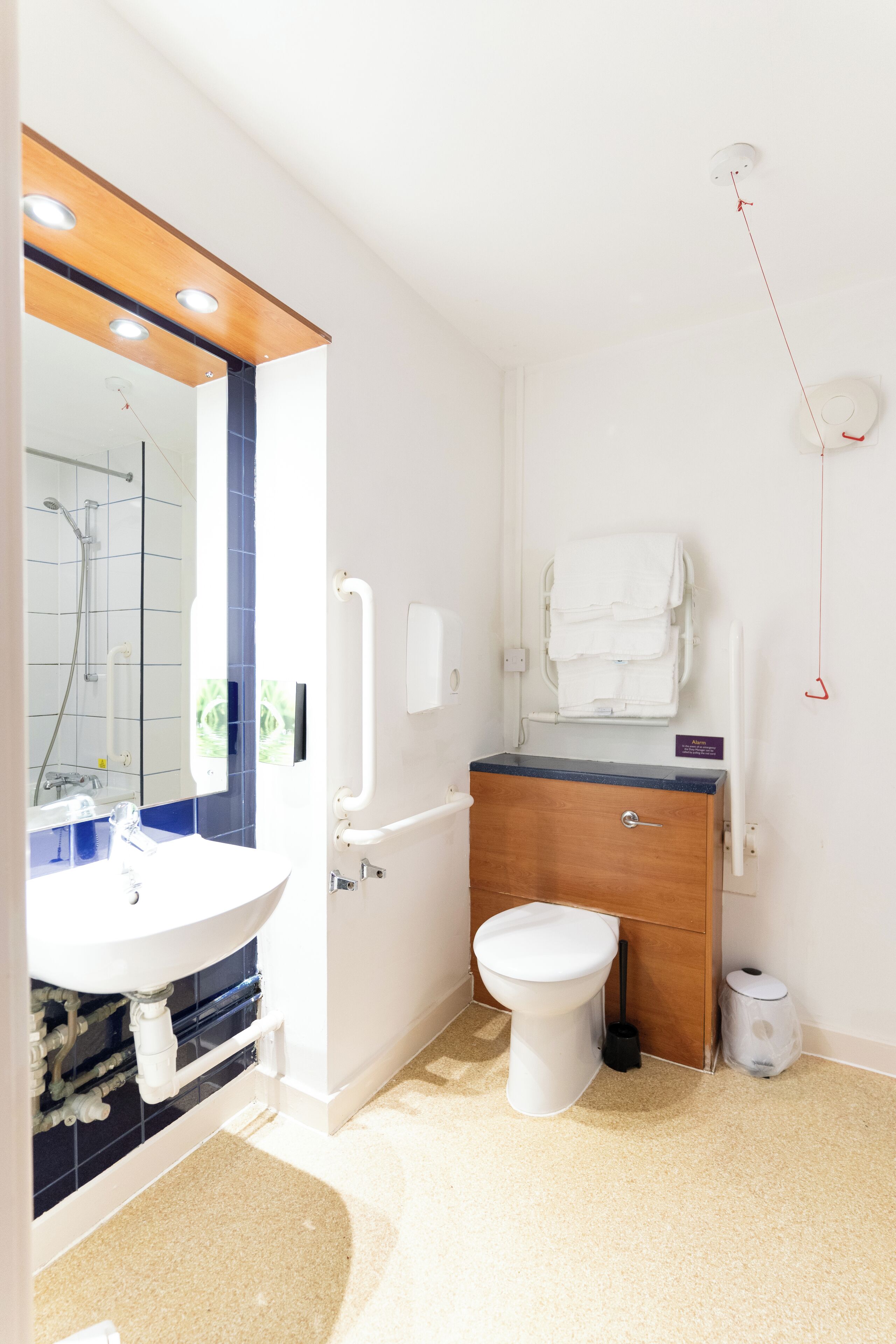 A modern bathroom with a white sink, a wooden vanity, a toilet, and a mirror with a wooden frame.
