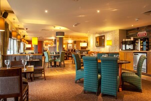 Un hall de hotel con varias zonas de estar, un bar y una cocina visible al fondo.