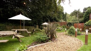 Un jardin avec un chemin de gravier, des bancs en bois et une clôture en bois.