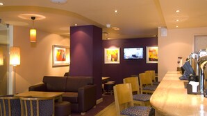 En hotellobby med en bar, en sittgrupp och tv-skärmar.