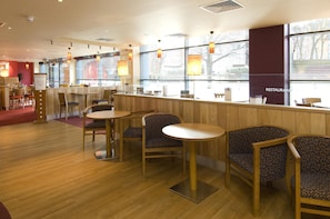 A restaurant with wooden tables and chairs, a counter, and large windows. - Premier Inn Leicester City Centre - Train Station (Leicester)