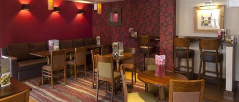 A hotel room with a sofa, dining table, chairs, and a patterned wall.