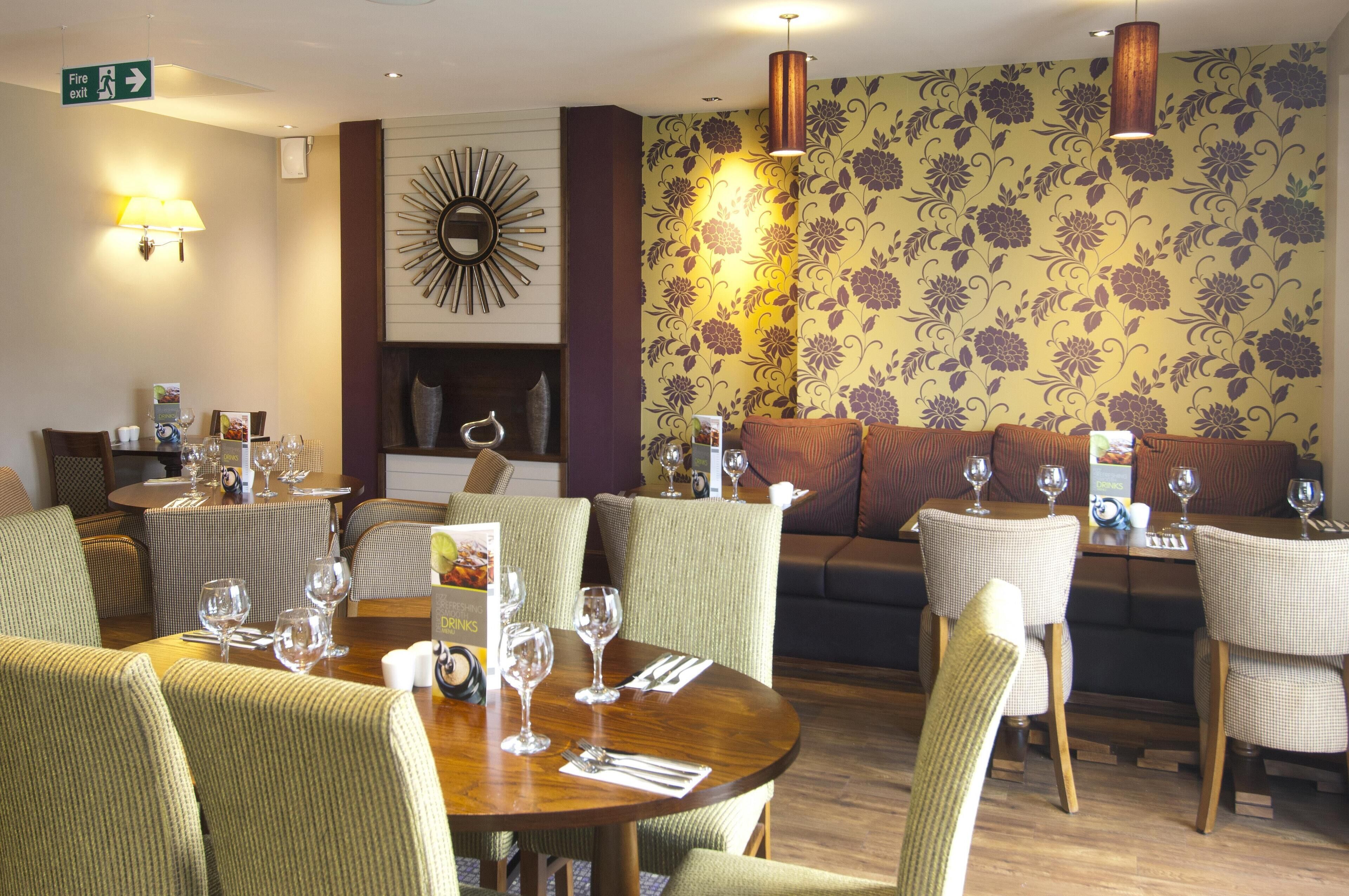 A dining area with round tables, chairs, and a sofa. There are wine glasses and a menu on the tables.