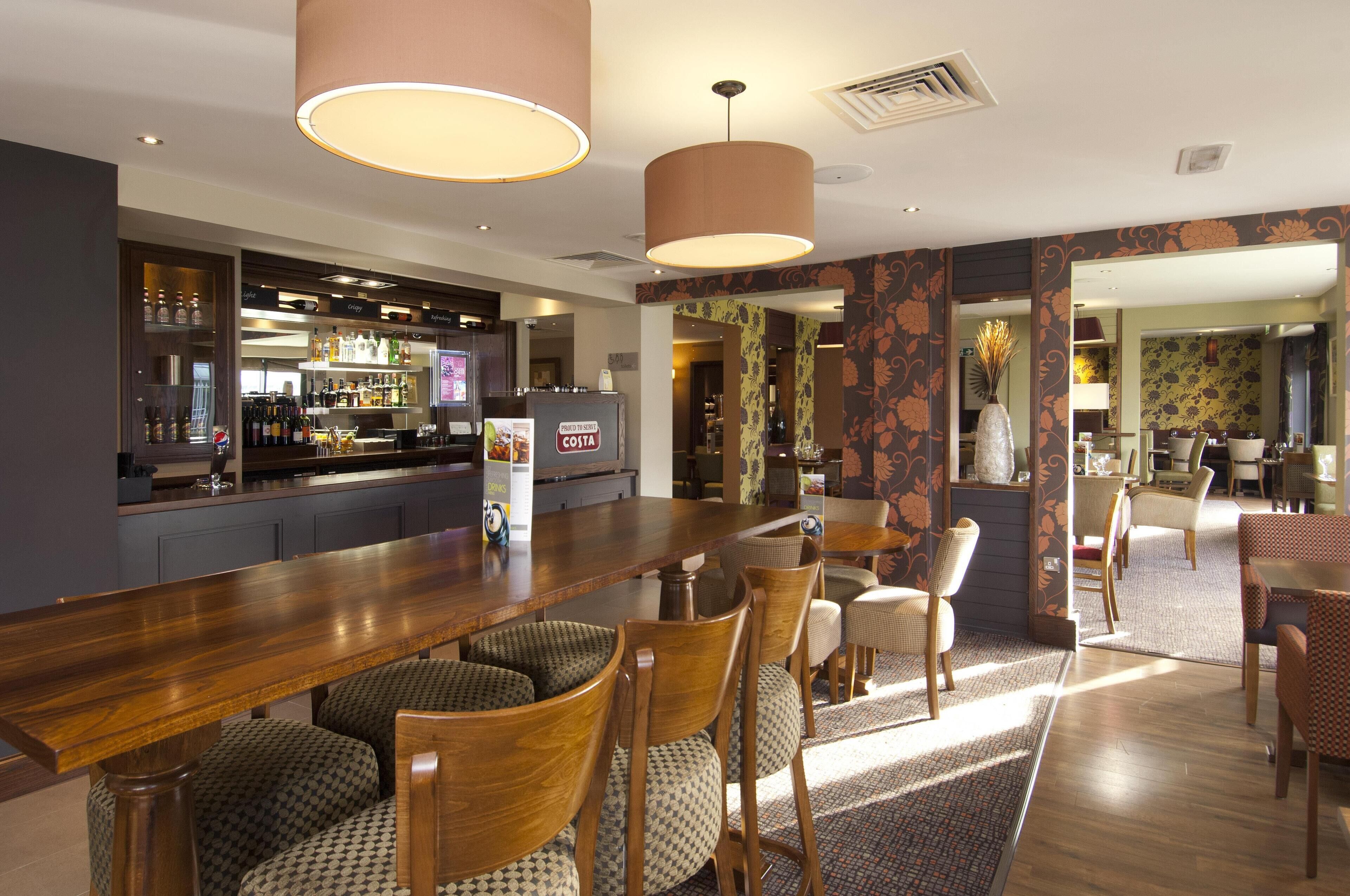 A bar area with a long wooden counter, bar stools, and a television screen.