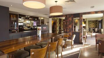 A bar area with a long wooden counter, bar stools, and a television screen.