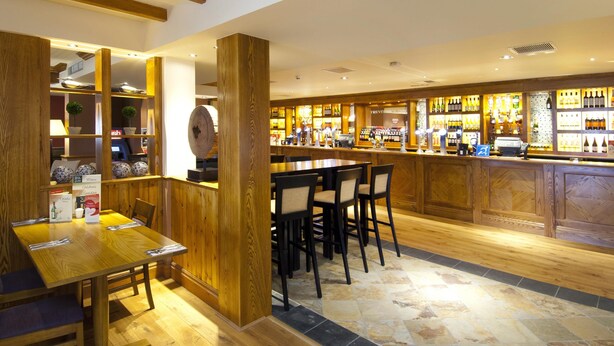 A bar area with wooden furniture, a counter with bottles, and a seating area with tables and chairs. - Premier Inn Camborne (Camborne)