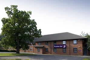 A brick building with a sign for Premier Inn, a parking lot, and a large tree.