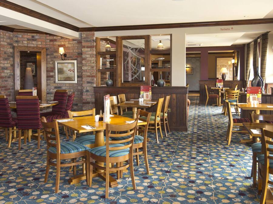 Un restaurant avec des tables et des chaises en bois, un sol à motifs, des murs en briques et un panneau indiquant la direction des toilettes.