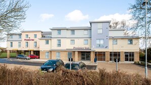 A hotel with multiple buildings, a parking lot with several cars, and a clear sky. - Premier Inn Witney (Witney)