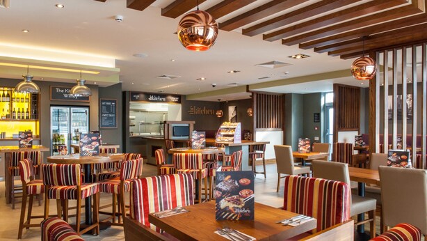 A restaurant with striped chairs, wooden tables, and hanging pendant lights. - Premier Inn Witney (Witney)