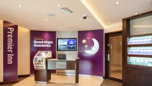 A hotel reception area with a check-in counter, a digital display, and a wall with a moon and stars design. - Premier Inn Witney (Witney)