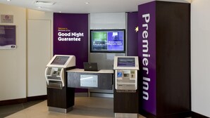 Een incheckruimte met een digitale kiosk, een televisiescherm en een 'Premier Inn'-bord.
