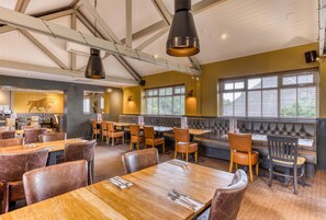 A restaurant with wooden tables and chairs, a high ceiling with exposed beams, and large windows. - Premier Inn Portsmouth North Harbour (Portsmouth)