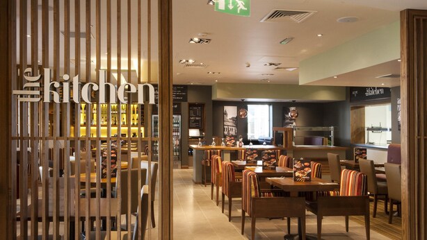 A restaurant interior with wooden partitions, tables, chairs, and a bar area. - Premier Inn Fleet (Fleet)