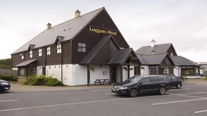 A building named 'Loggans Moor' with a dark brown exterior, a pitched roof, and a welcoming sign. - Premier Inn Hayle (Hayle)