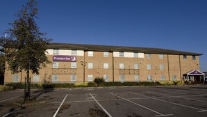 A multi-story hotel with a parking lot in front, a sign for Premier Inn, and a small building with a purple roof. - Premier Inn Ashford Central (Ashford)