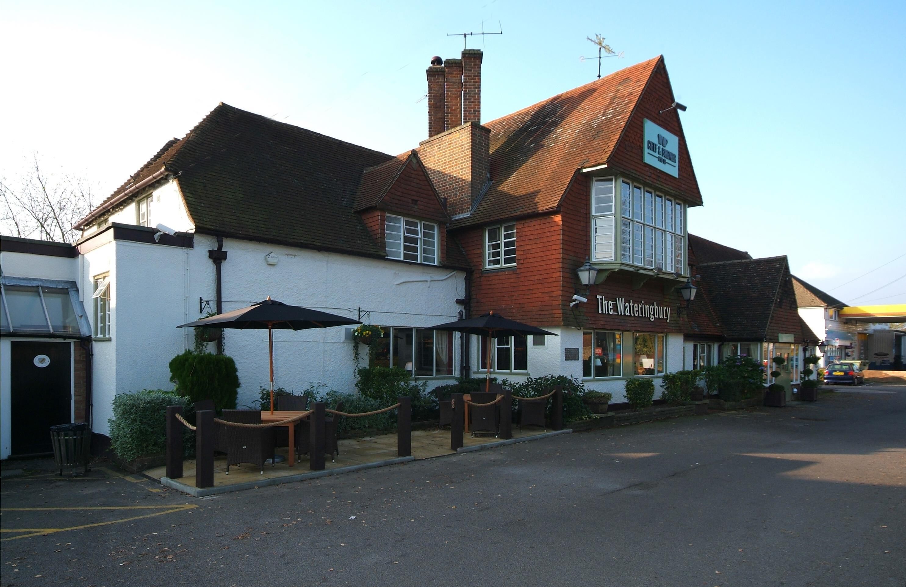 A traditional pub with outdoor seating, a sign reading 'The Wateringbury,' and a clear sky.