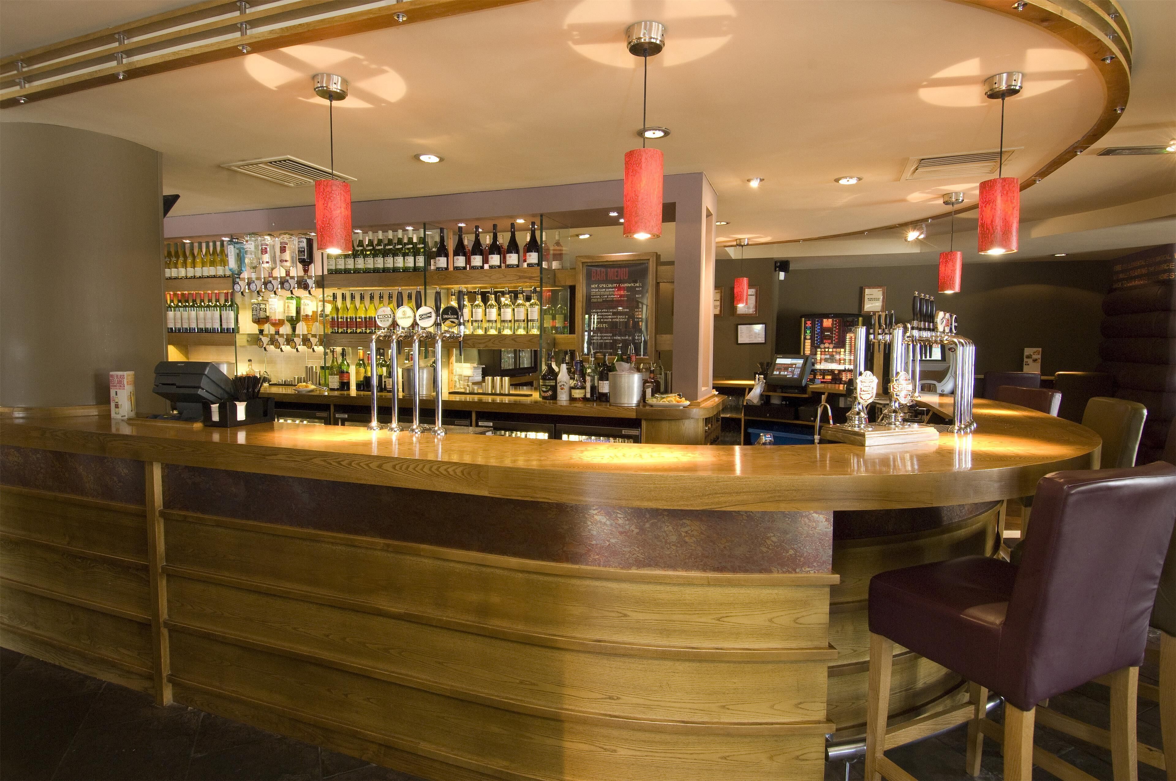 Zona de bar con mostrador de madera, varias botellas y una pizarra con la carta.
