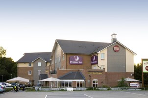 Un hotel con un llamativo letrero de Premier Inn, fachada de ladrillo y un área de estar al aire libre cubierta.