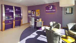 Zona de recepción de Premier Inn con mostradores de registro, sillas, un escritorio y un cartel en la pared.