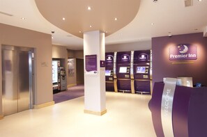 A hotel reception area with a 'Welcome' sign, a digital check-in kiosk, and an elevator. - Premier Inn Rochester (Rochester)