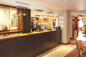 A bar area with a counter, bar stools, and a variety of bottles. - Premier Inn Rochester (Rochester)