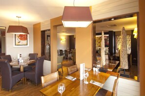 A restaurant with wooden tables and chairs, a hanging light fixture, and a framed artwork on the wall. - Premier Inn Rochester (Rochester)