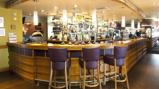 A bar area with a curved counter, bar stools, and overhead lighting. - Premier Inn Swanley (Swanley)