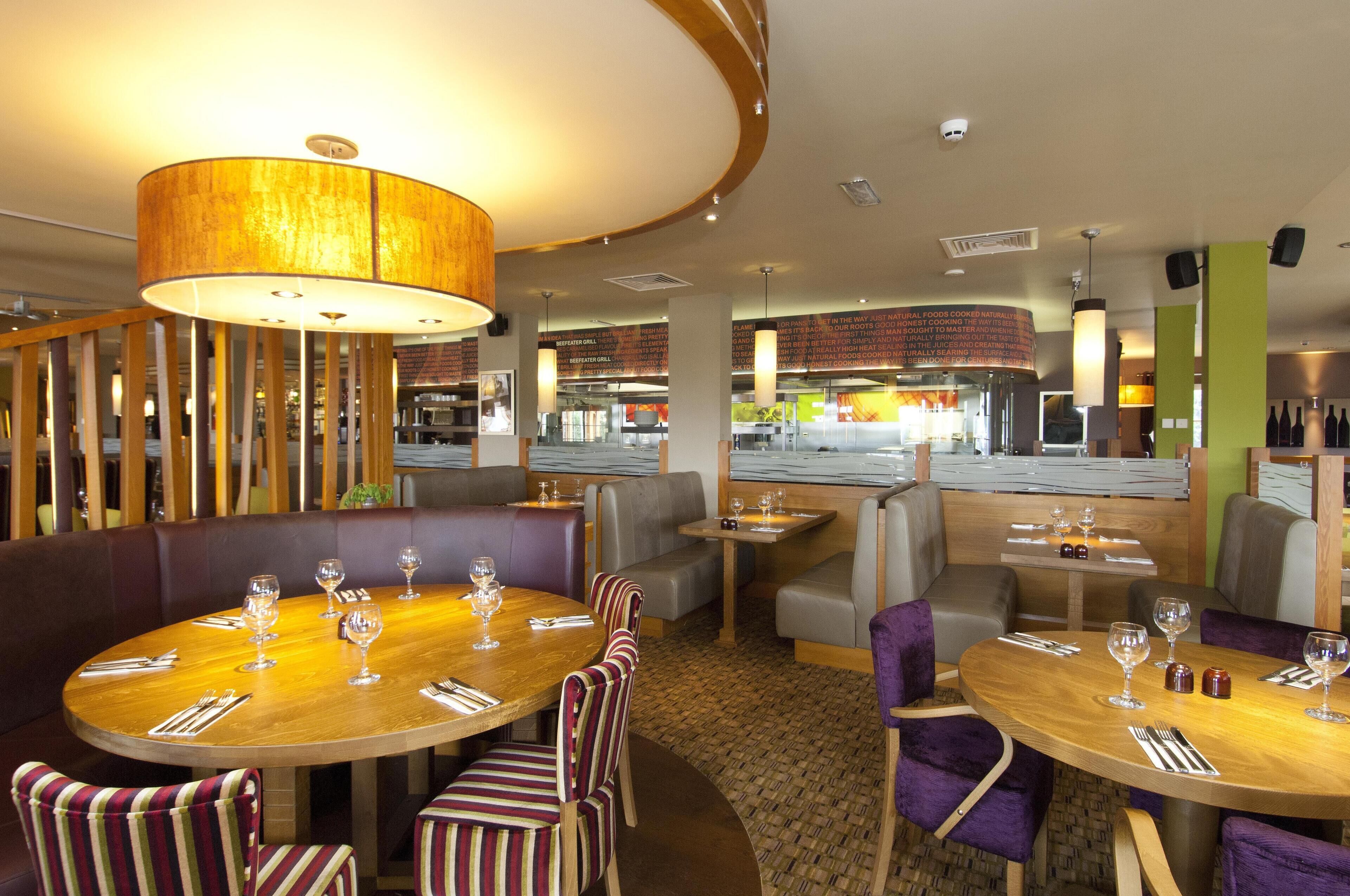A restaurant with round tables, striped chairs, and a large hanging light fixture.