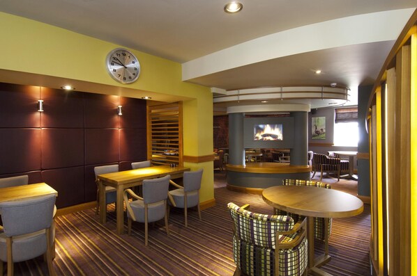A hotel lobby with a clock, seating areas, a fireplace, and a view of the outdoors. - Premier Inn Swanley (Swanley)