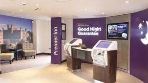 Un espace d’accueil Premier Inn doté d’un kiosque d’enregistrement numérique, d’un coin salon et d’un écran mural affichant les informations relatives à la « Garantie d’une bonne nuit ».