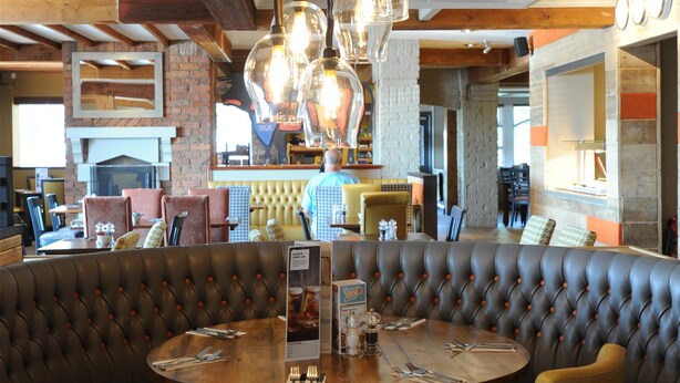 Restaurante com mesa redonda, assentos em cabines de couro e luminárias pendentes.