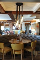 A restaurant with a round table, leather booth seating, and hanging pendant lights.