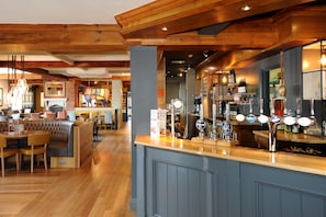A bar area with wooden beams, a counter with multiple taps, and a seating area with a cushioned bench. - Premier Inn Southend Airport (Southend-on-Sea)