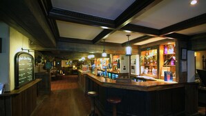 Zona de bar con suelo de madera, taburetes y una barra que exhibe varios objetos.