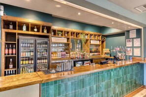 A bar area with shelves of bottles and glasses, a refrigerated display, and a wooden counter. - Premier Inn Southampton City Centre (Southampton)