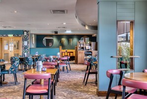 A restaurant with round tables and chairs, a wooden counter, and a mirror on the wall. - Premier Inn Southampton City Centre (Southampton)