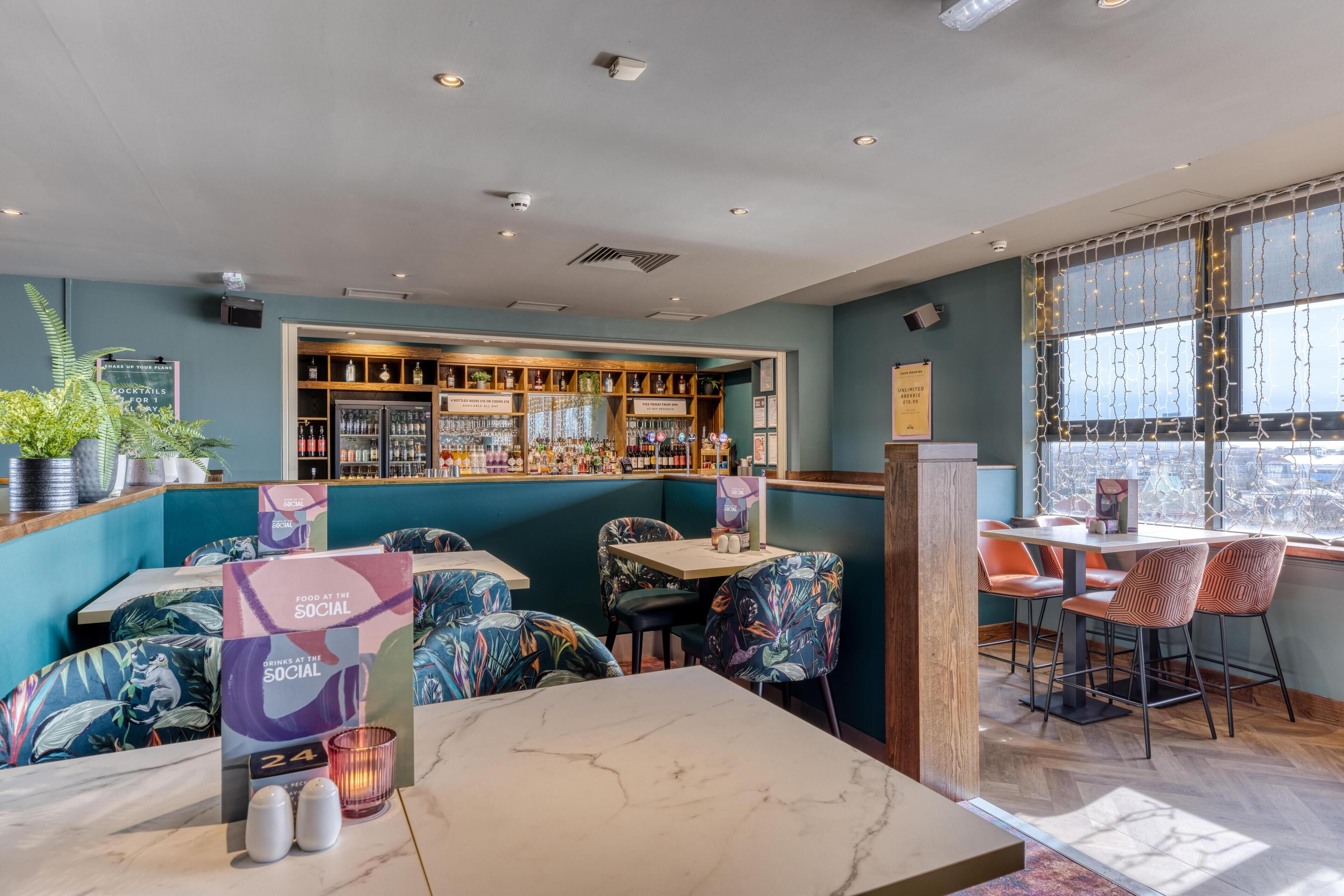 A restaurant with a bar area, seating with patterned chairs, and a view through the window.