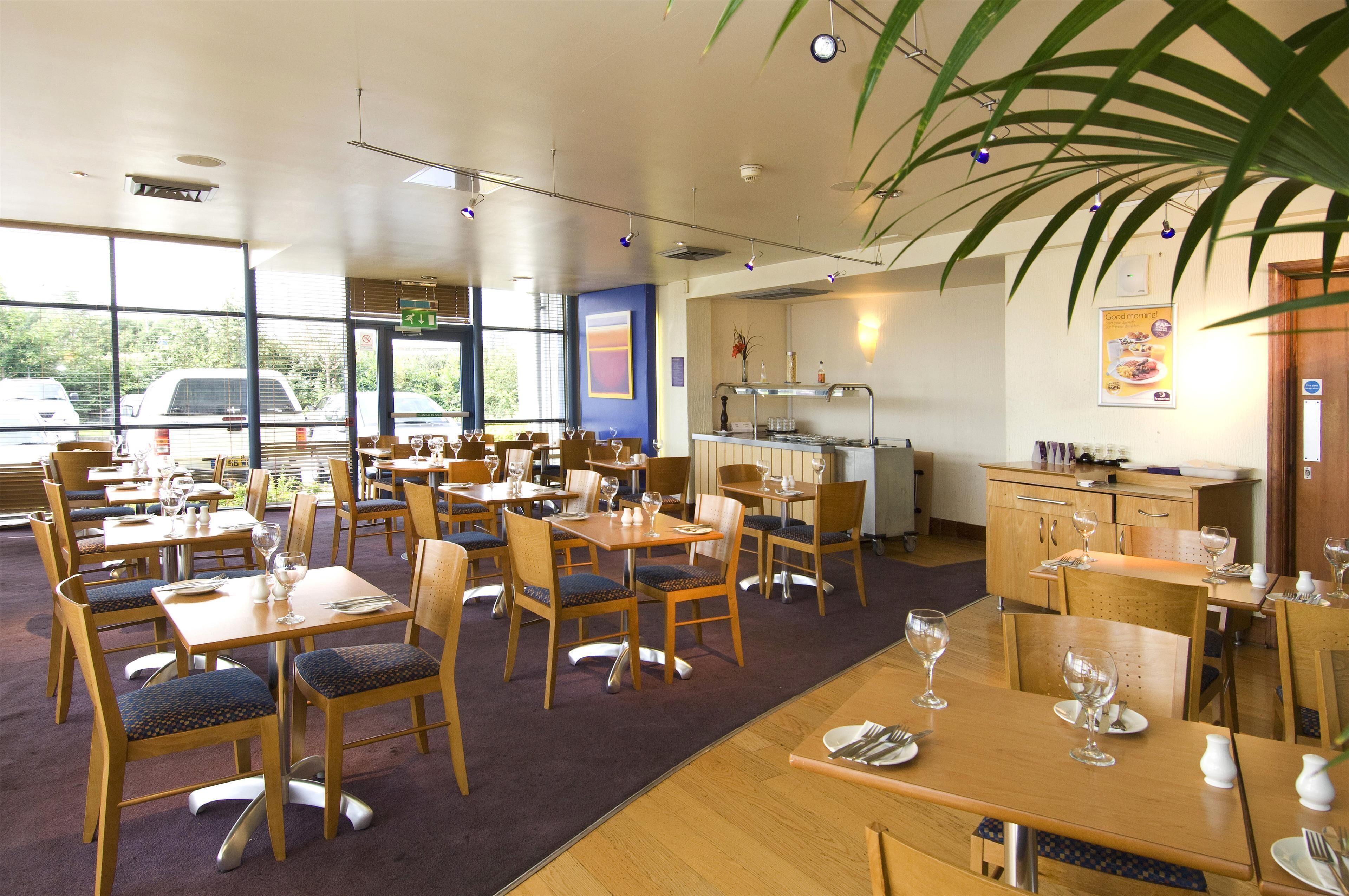 A restaurant with multiple tables and chairs, a kitchen area, and large windows.