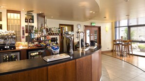 Eine Bar mit einer Theke, verschiedenen Flaschen, einem Kühlschrank und einer Kaffeemaschine.