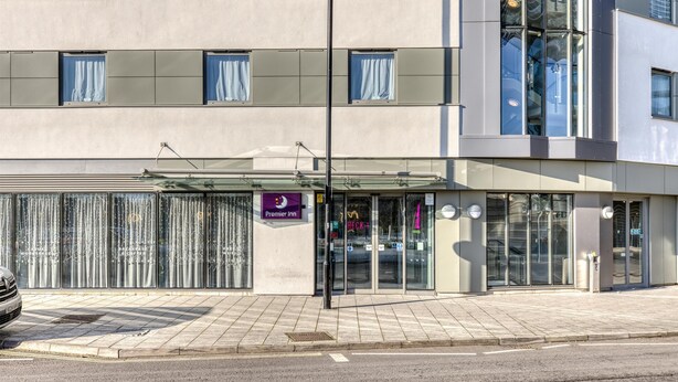 Ein Hotel mit Glastür, einem sichtbaren Schild für Premier Inn und einem parkenden Auto davor.