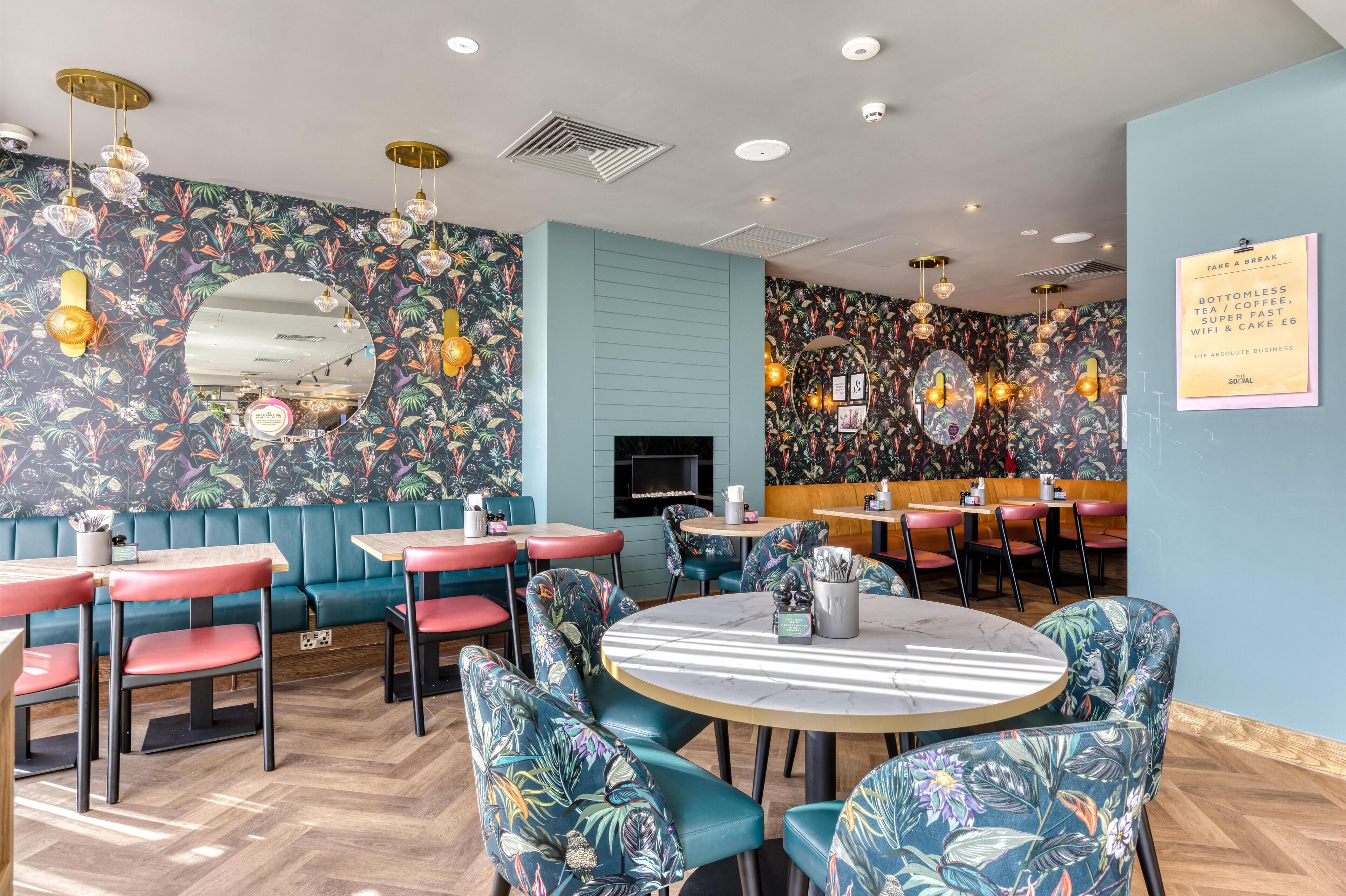 Een restaurant met zitjes en tafels, bloemenmotieven op de wanden, en een bord waarop staat dat er onbeperkt thee, koffie en Wi-Fi beschikbaar is.