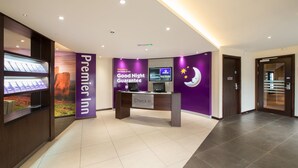 A Premier Inn reception desk with a 'Good Night Guarantee' sign, a digital screen, and a reception area with a tiled floor. - Premier Inn Stourbridge Town Centre (Stourbridge)